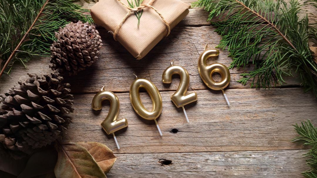 Gold 2026 candles with gift, pinecone, and greenery on rustic wood surface.