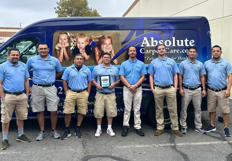 Group of men in blue shirts and khaki shorts standing in front of a blue Absolute Carpet Care van.