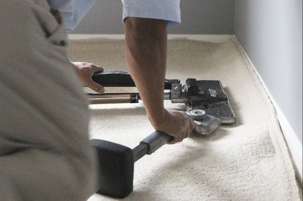 A man is cleaning a carpet with a vacuum cleaner