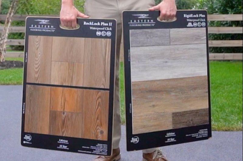 A man is holding two boards with different types of wood on them.