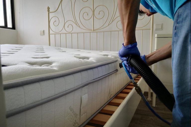 A man is cleaning a mattress with a vacuum cleaner