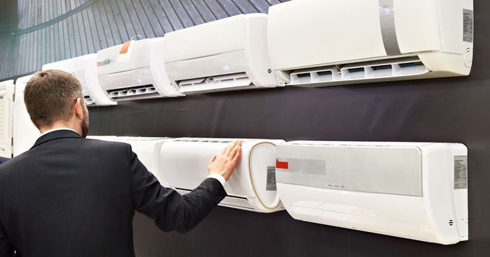 A man in a suit is standing in front of a wall of air conditioners.