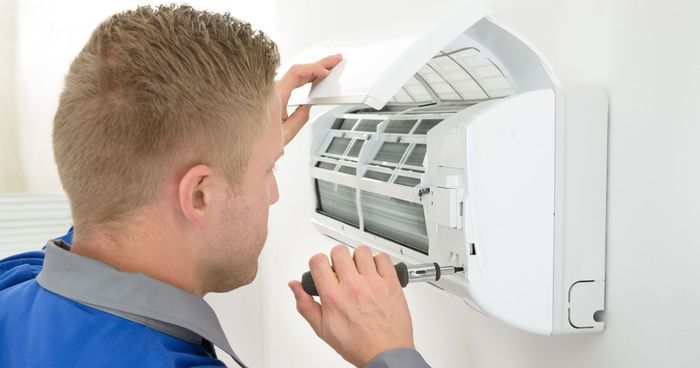 A man installing an air conditioner with a screwdriver.