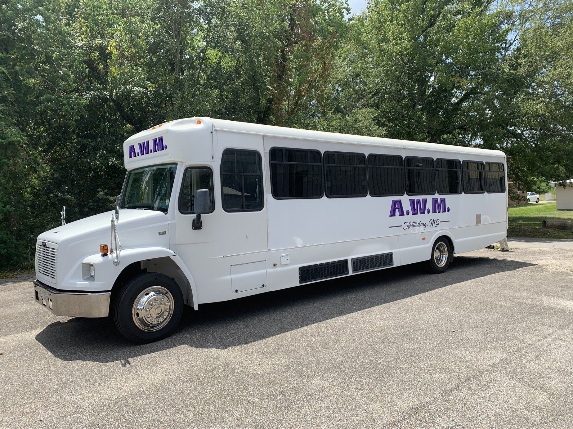 A white bus is parked in a parking lot with trees in the background.