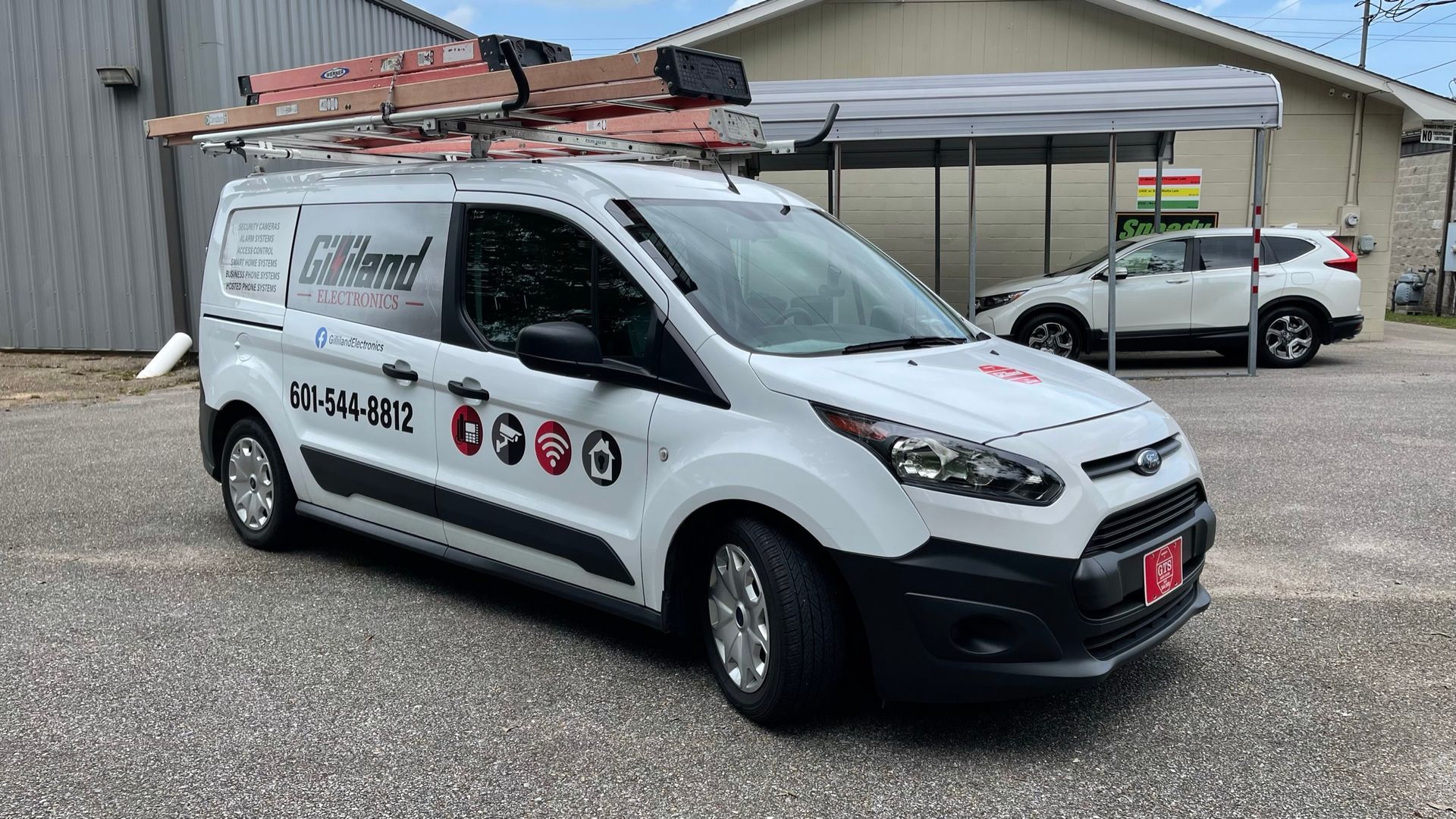 A white van with a ladder on top of it is parked in front of a building.