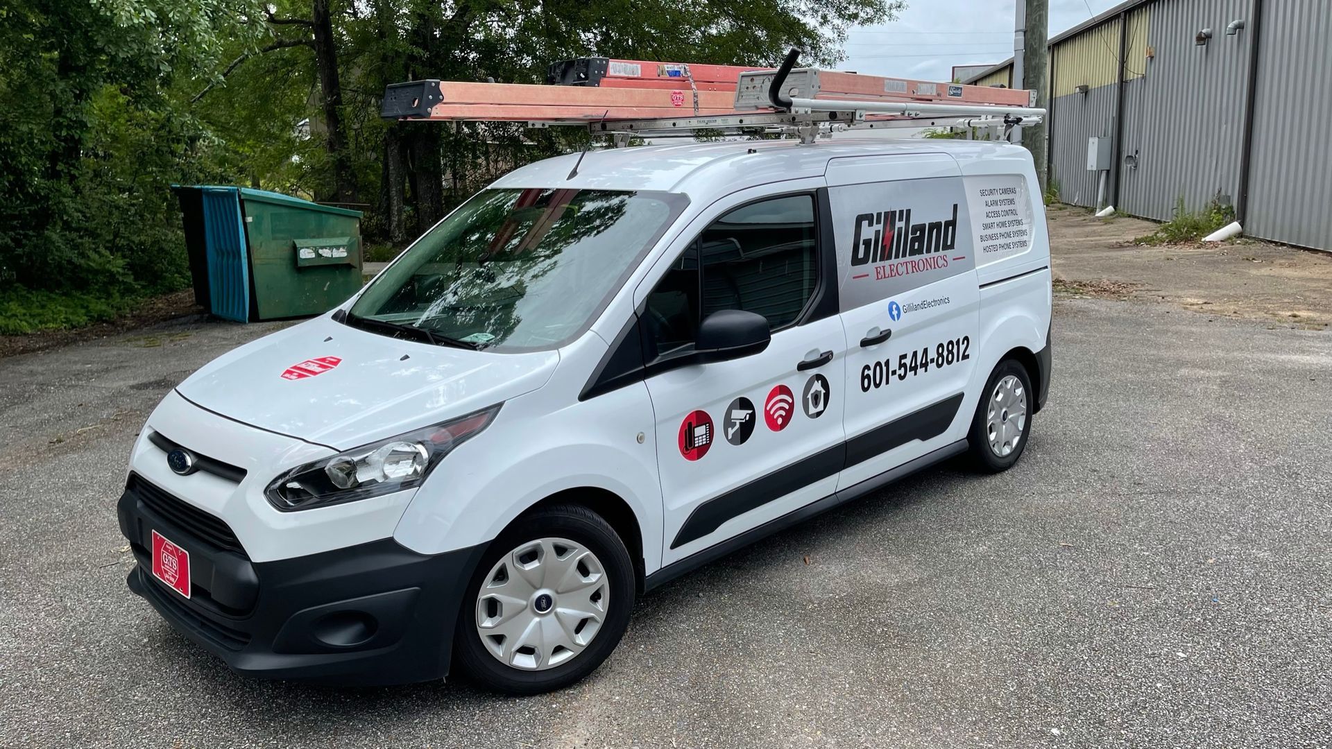 A white van with a ladder on top of it is parked in a parking lot.
