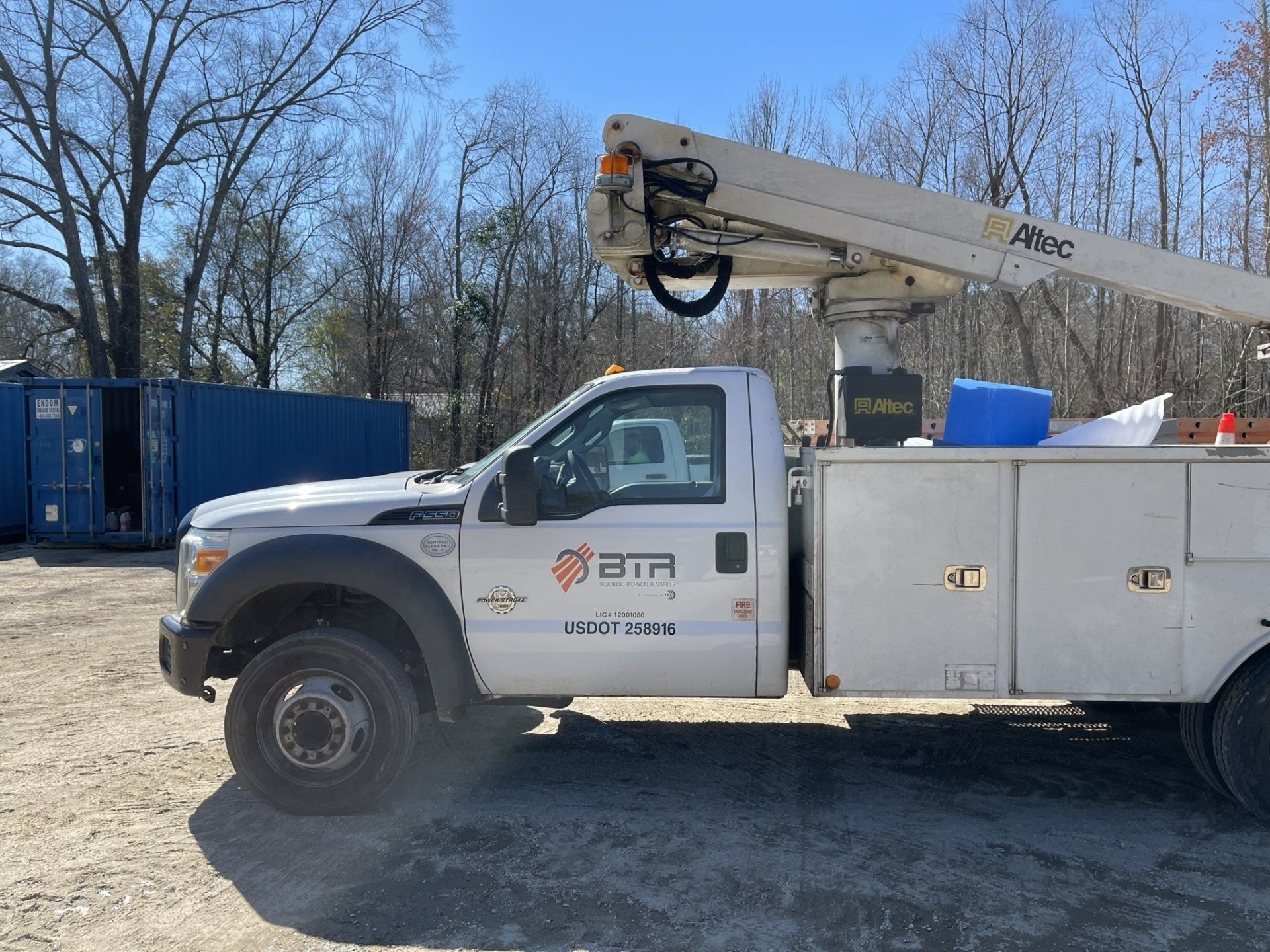 A white truck with a crane on top of it is parked in a dirt lot.