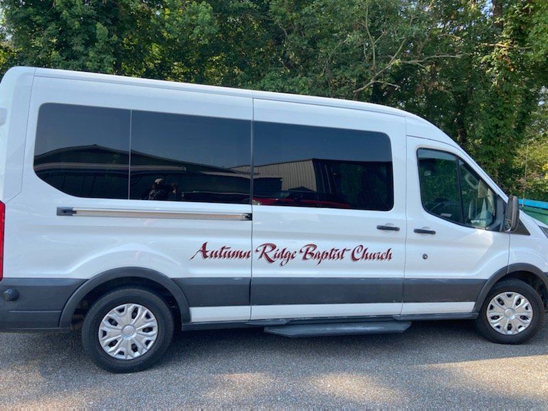 A white van with autumn ridge baptist church written on the side is parked in a parking lot.