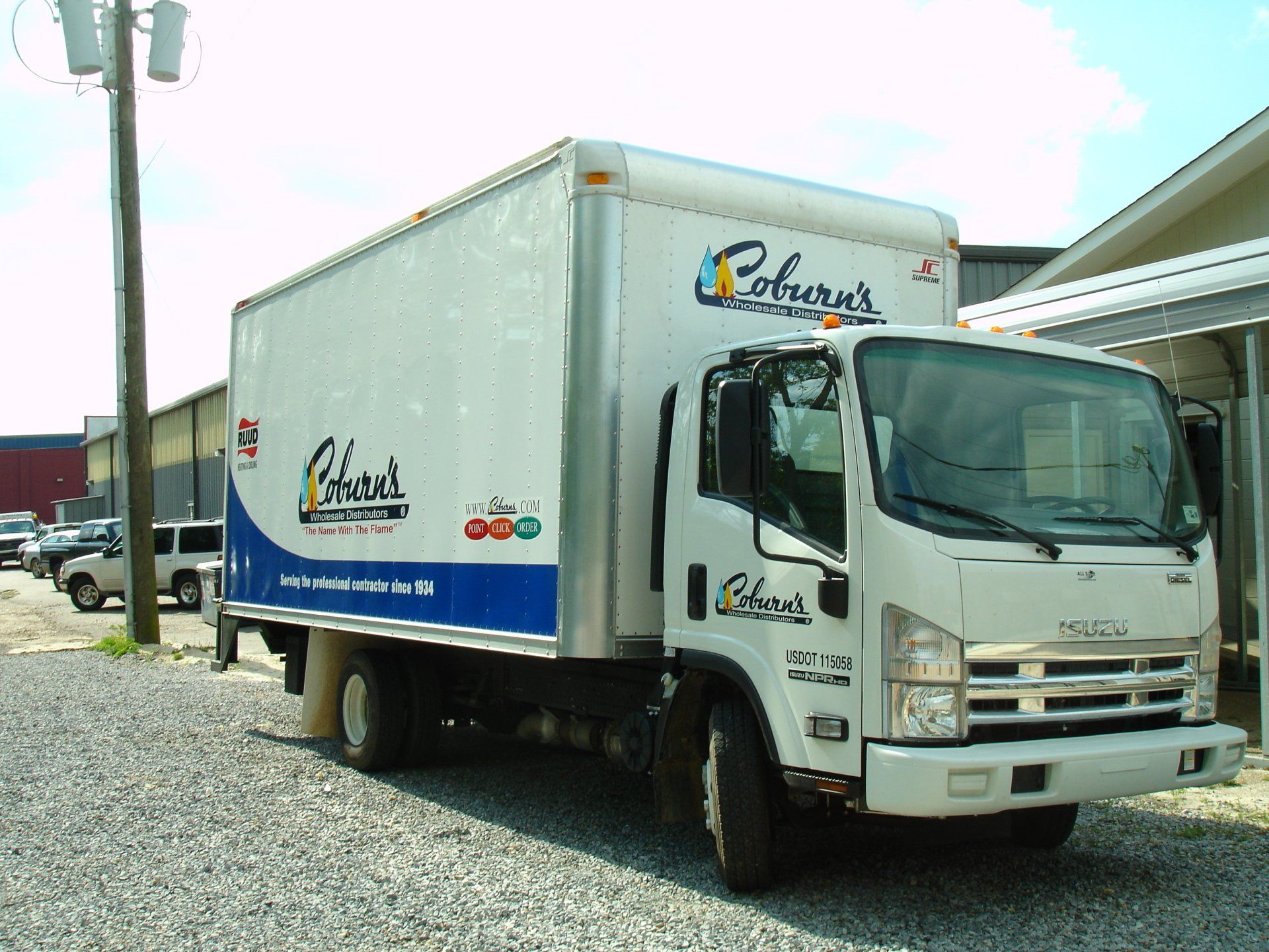 A white and blue coburn 's truck is parked in a gravel lot