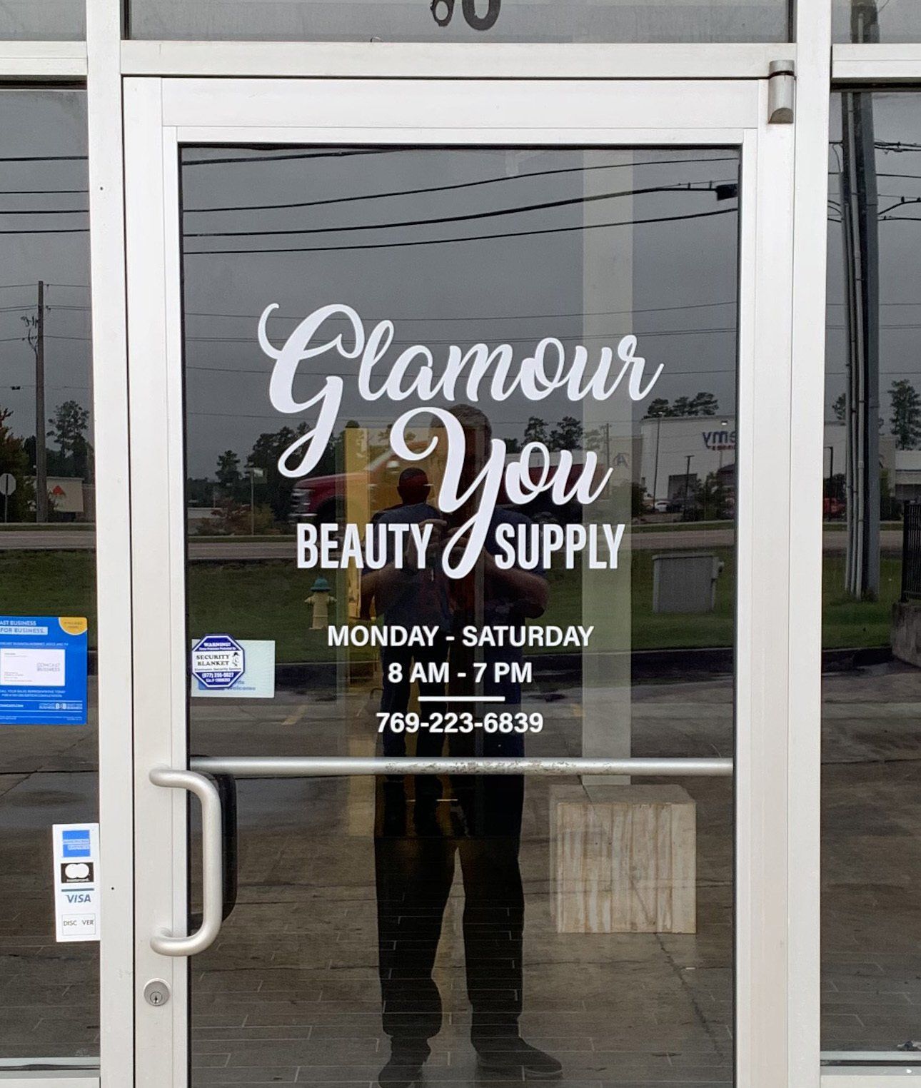 A man is standing in front of a door that says glamour you beauty supply
