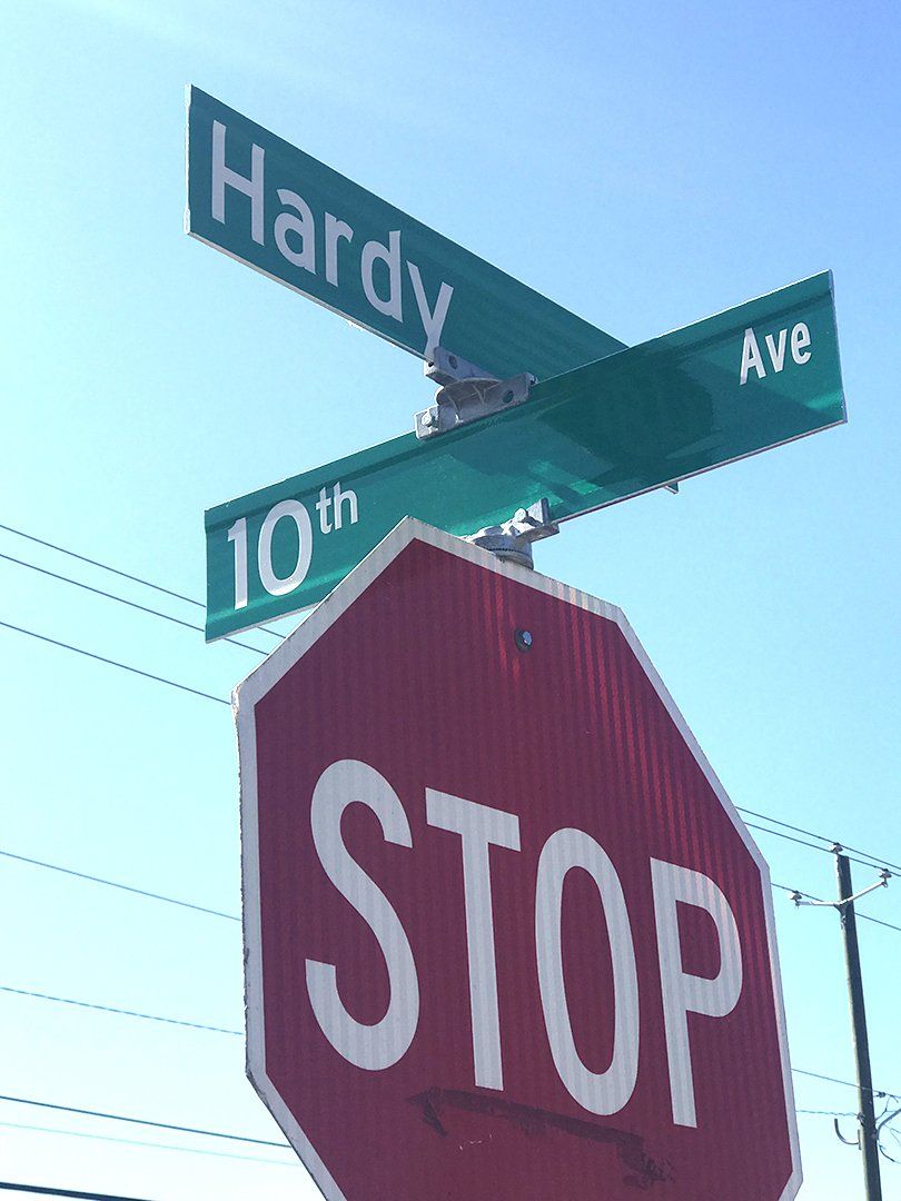 A stop sign is under a street sign for hardy ave