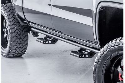 Black truck with side steps and large, black tires. Steps are made of black metal.