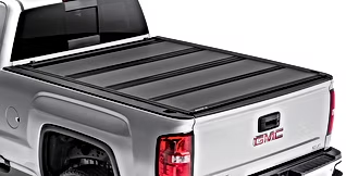 Silver GMC truck with a black, folding tonneau cover. Tailgate is closed.