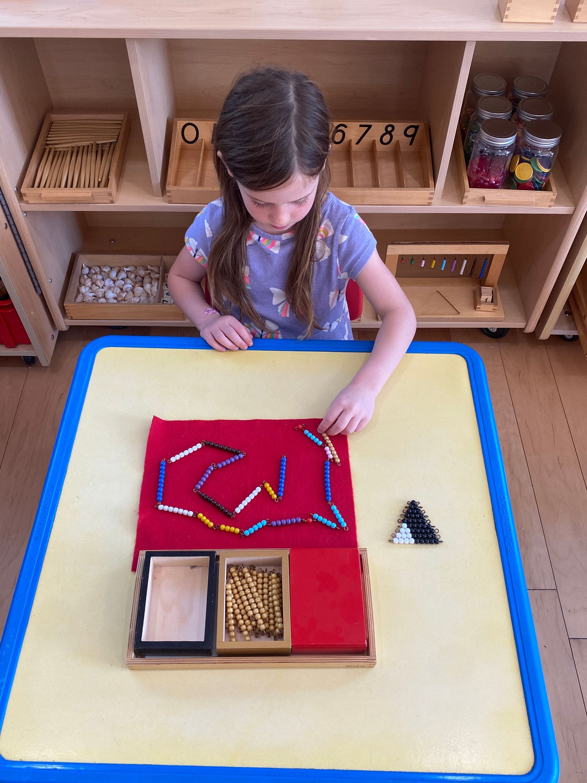 Girl at table using Montessori materials: colored beads, blocks, and wooden shapes.