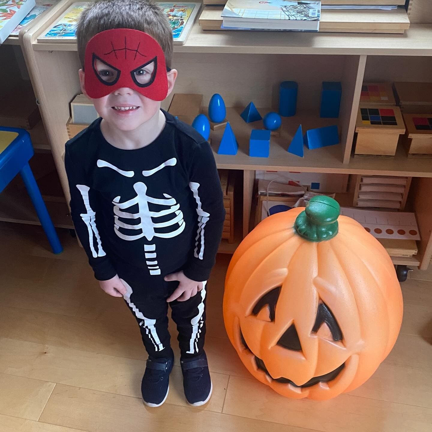 Child in skeleton costume and Spider-Man mask beside a large jack-o'-lantern.