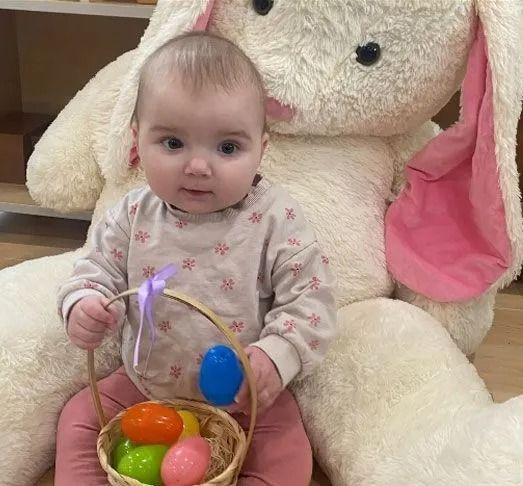 Baby holding Easter basket, sitting in front of a giant stuffed bunny.