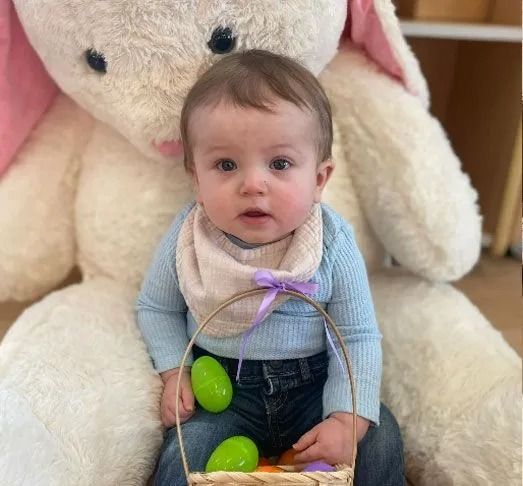 Baby sitting in front of a giant stuffed bunny holding a basket of Easter eggs.