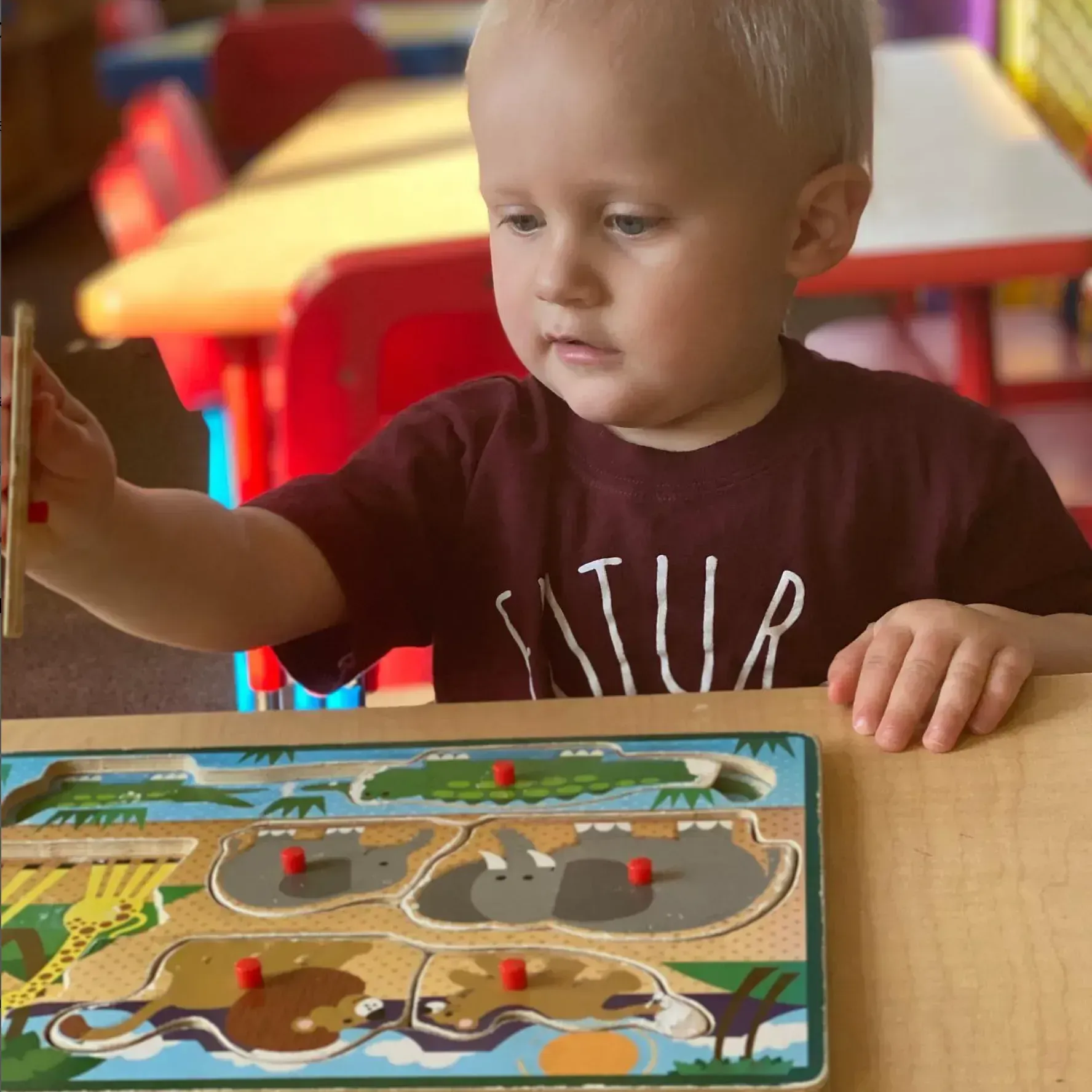 Child playing with a zoo animal puzzle at a table, looking intently, indoor setting.