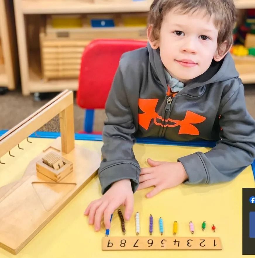 Boy at table with Montessori materials: ramp, rods, wooden numbers. Smiling, indoors.