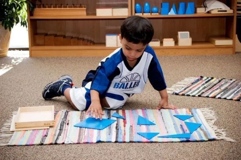 Boy using blue geometric shapes on a rug in a classroom setting.