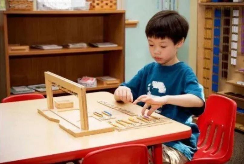 Boy using Montessori math materials at a table in a classroom.