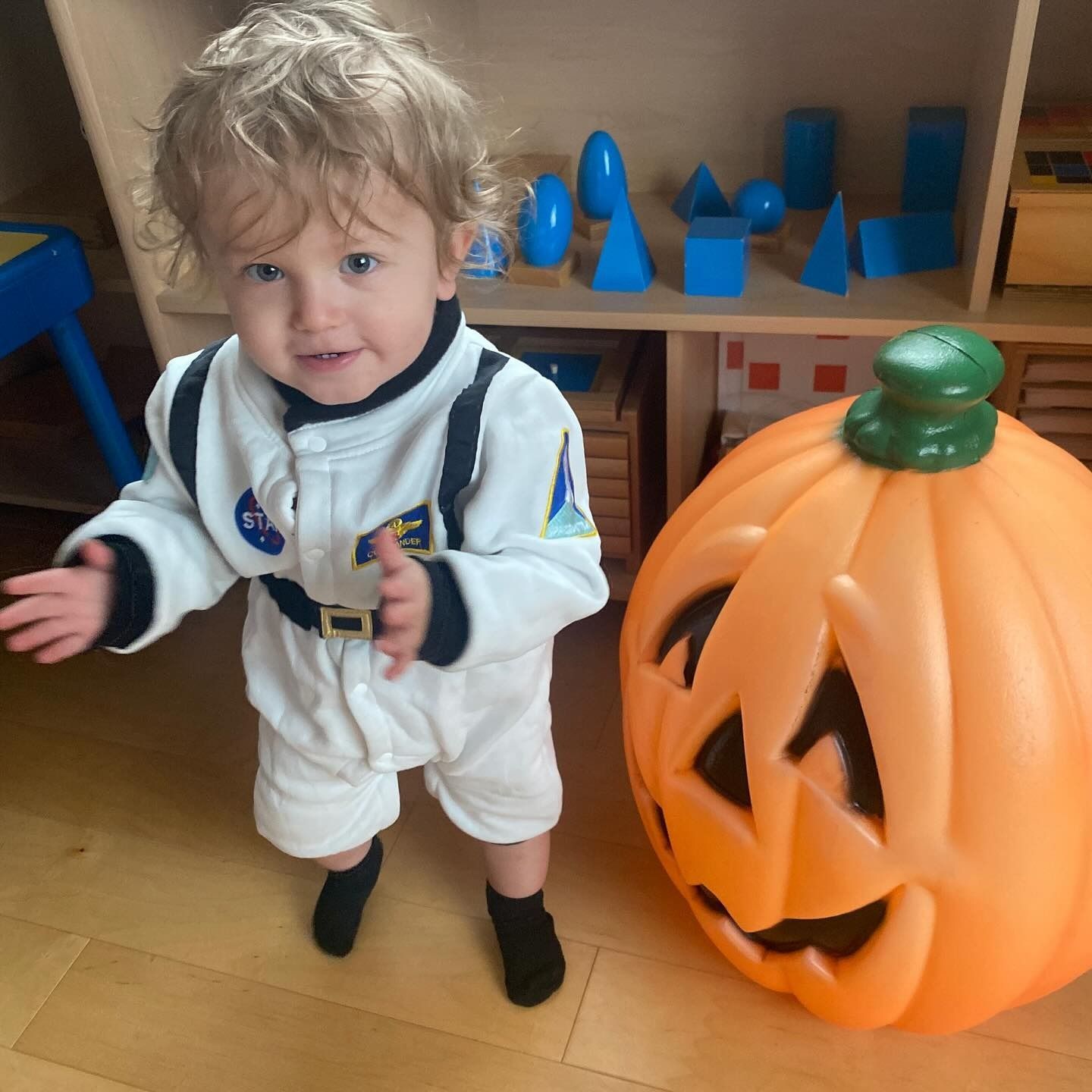 Child in astronaut costume stands next to a large plastic jack-o'-lantern.