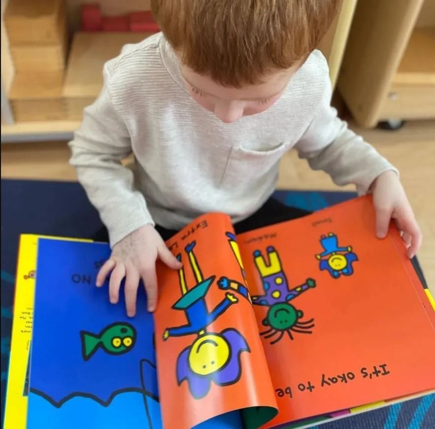 Child reading a colorful book, with cartoon figures, indoors.