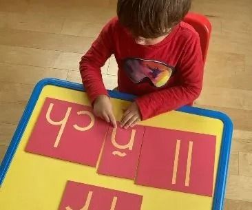 Boy arranging pink letter cards on a yellow table.