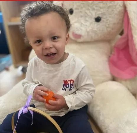 Child smiles, holding a toy, near a large stuffed bunny.