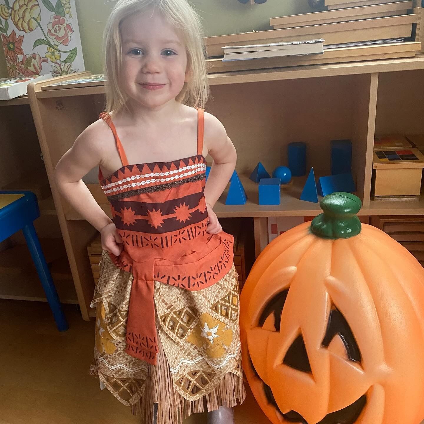 Girl in Moana costume poses next to a large orange pumpkin.