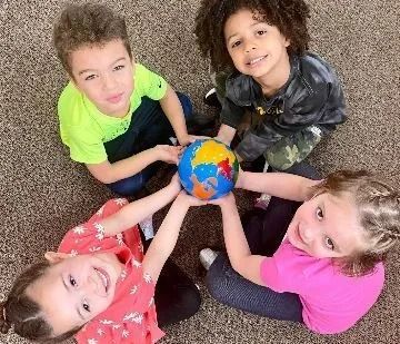 Four children holding a globe, smiling, sitting on a carpet.