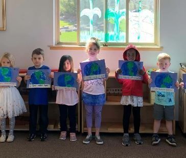Children holding Earth Day artwork in front of a window. Blue, green, and white.