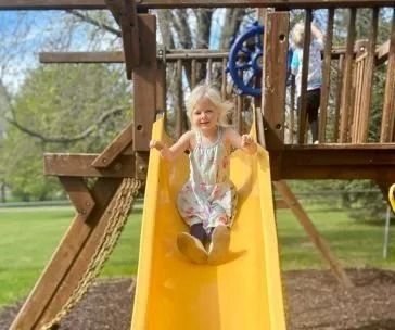 Young child slides down a yellow slide on a wooden playground.