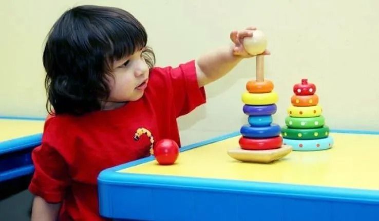 Child in red shirt stacking colorful rings on wooden toy.
