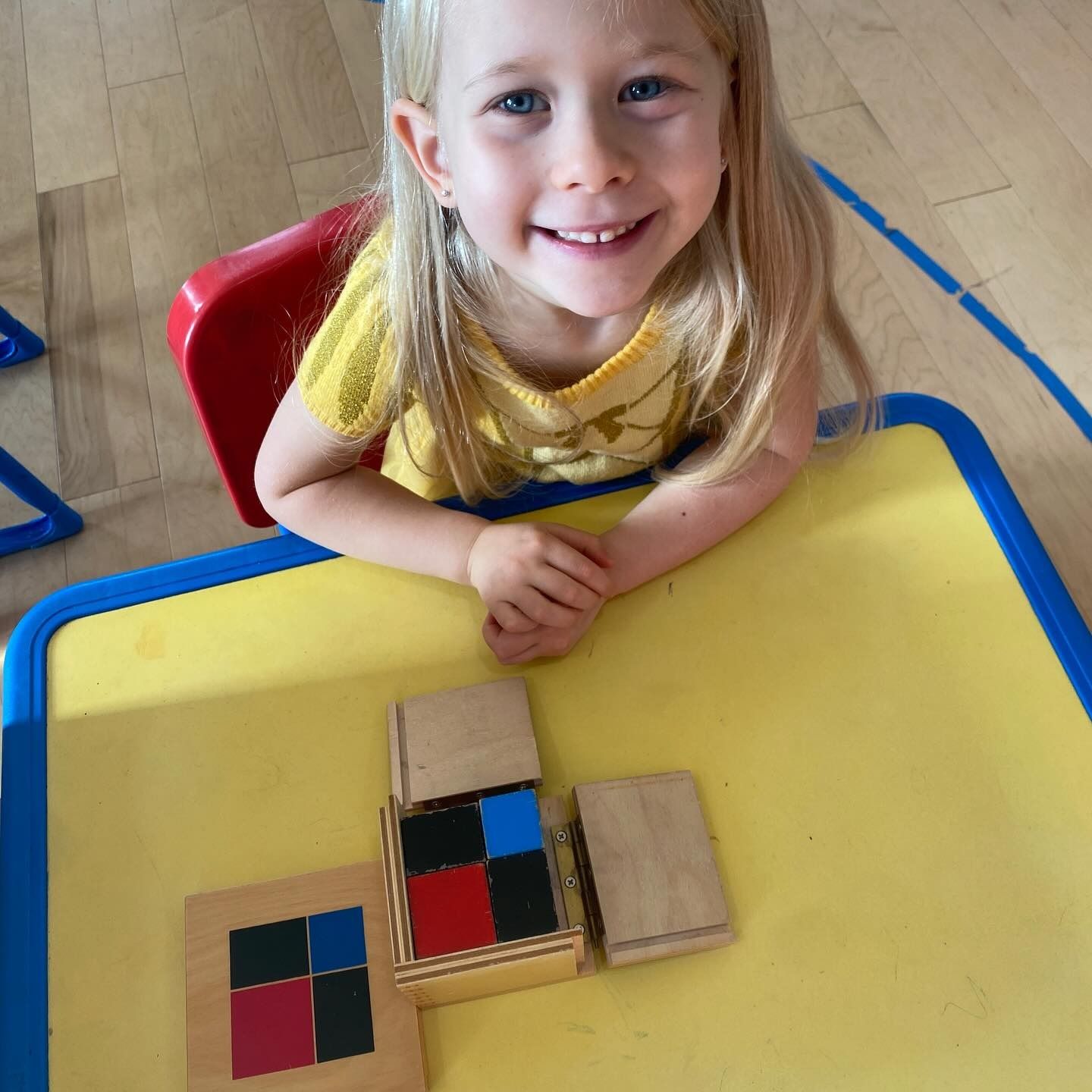 Young child smiles, playing with colorful blocks on a yellow table.