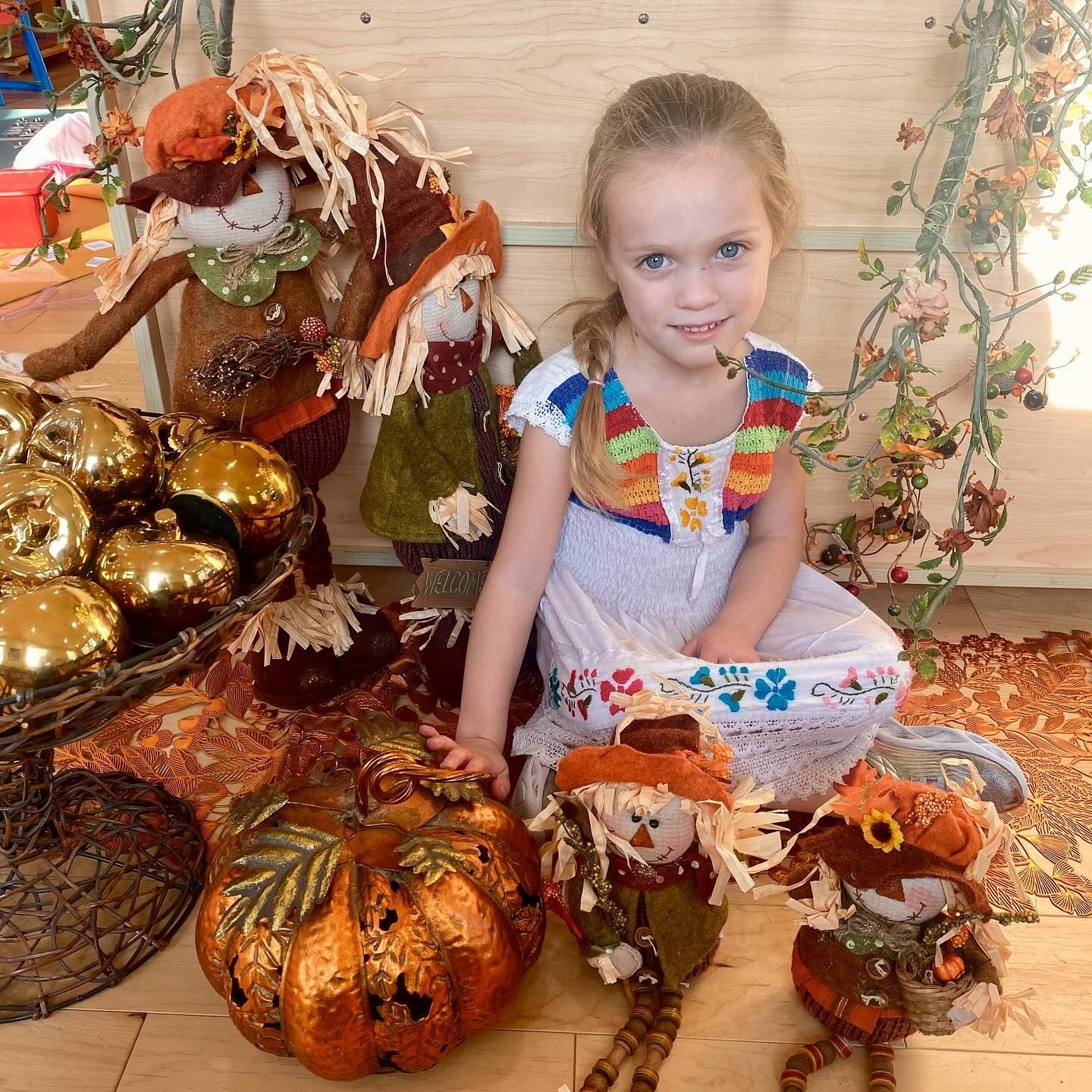 Young girl poses with autumn decorations, including pumpkins and scarecrows.