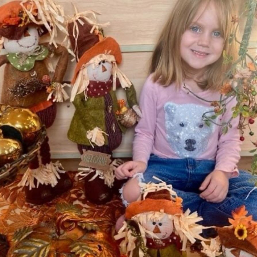 Girl smiling with scarecrows and autumn decor.