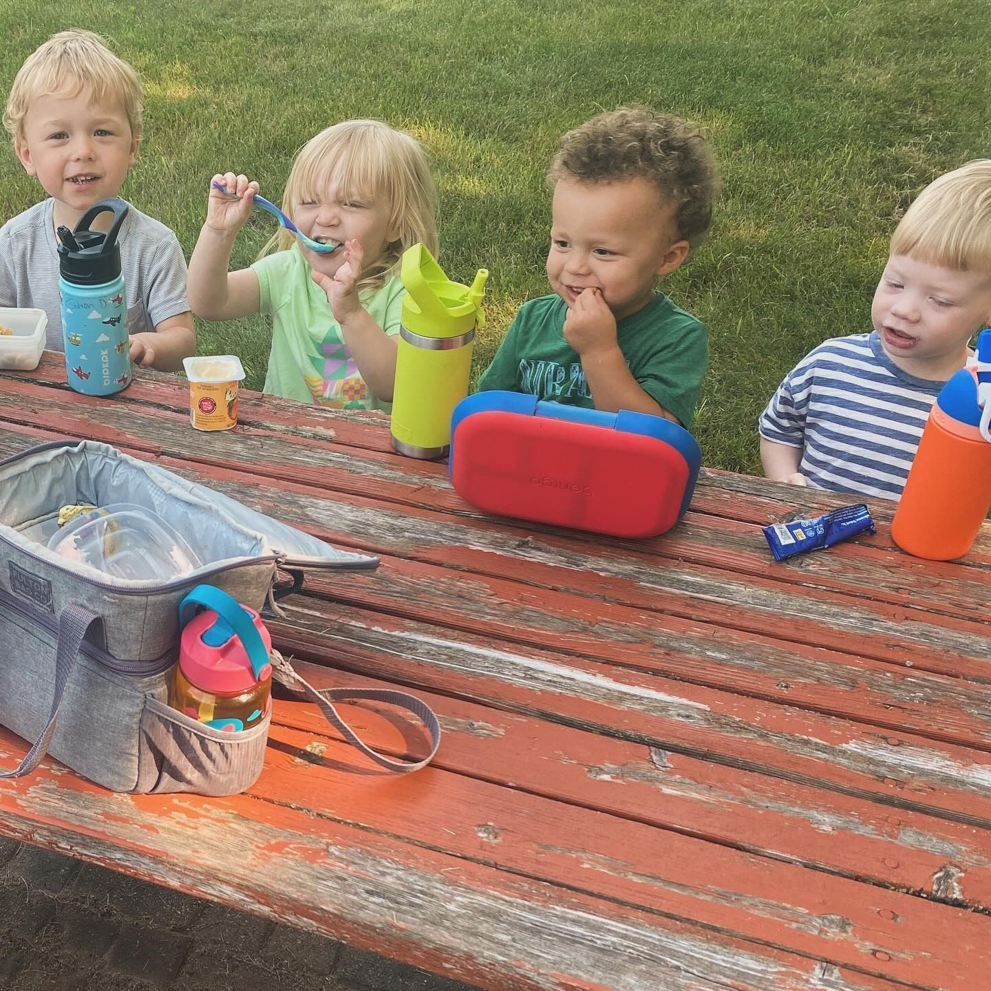 Children eating snacks at a red picnic table outdoors.
