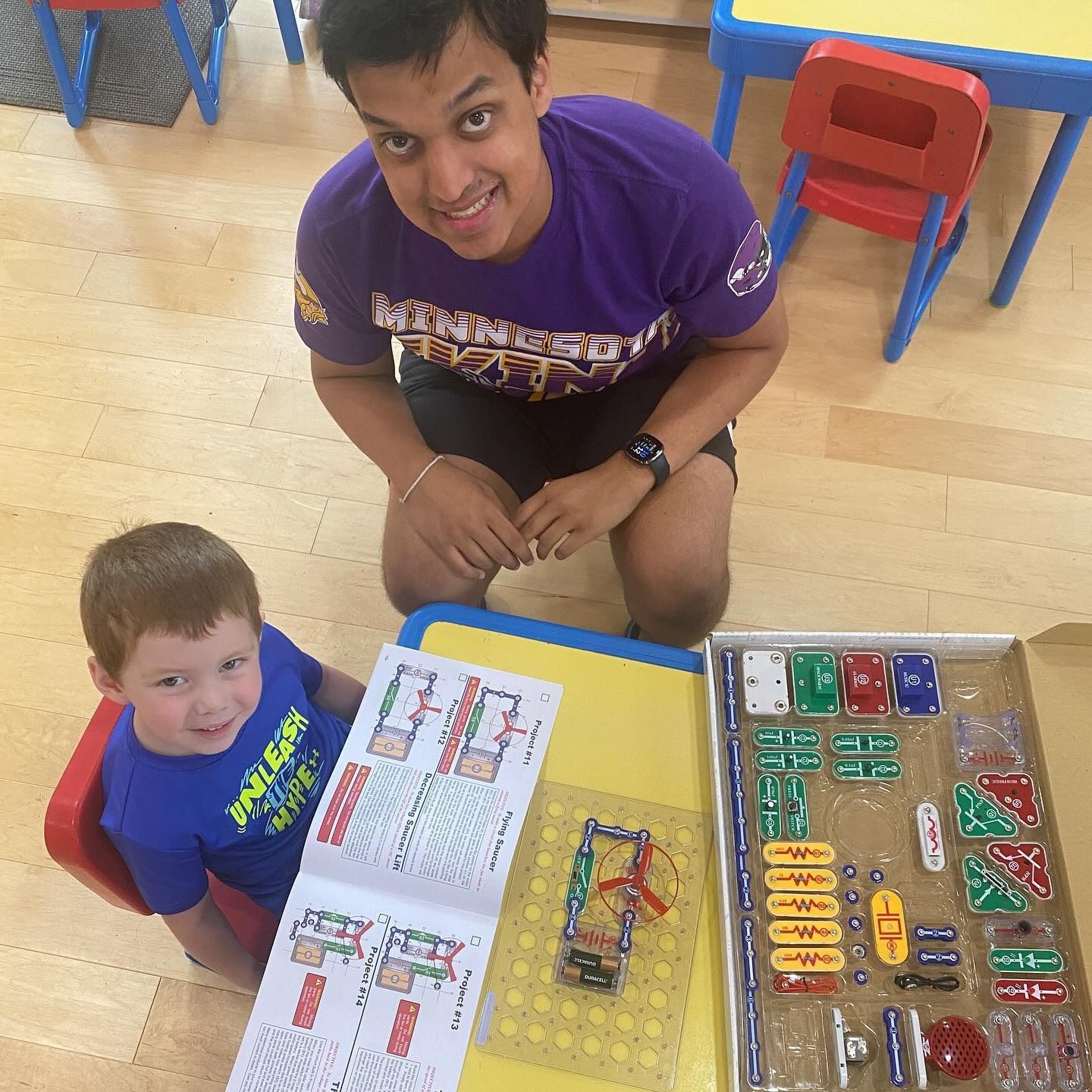 Man and child building circuits with electronic components. They are seated at a table indoors.