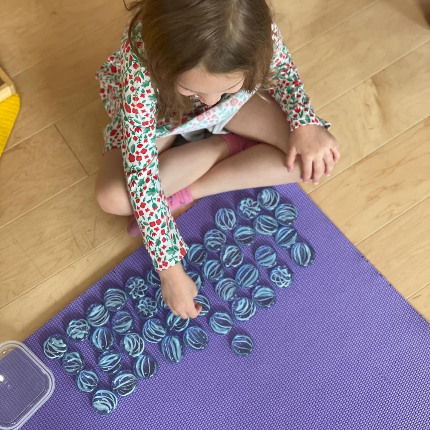 Young child sits on a purple mat arranging blue and white striped game pieces on a wood floor.