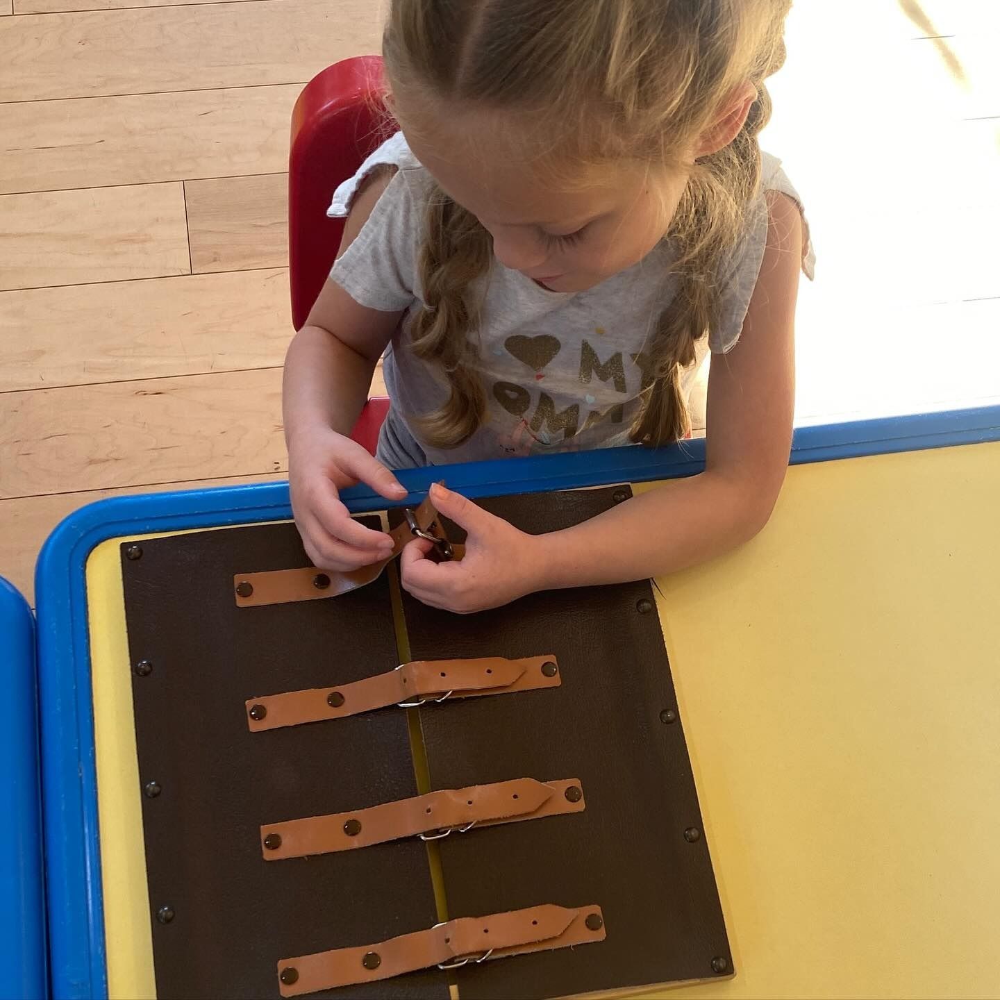 A child concentrates on manipulating buckles on a wooden board at a table.