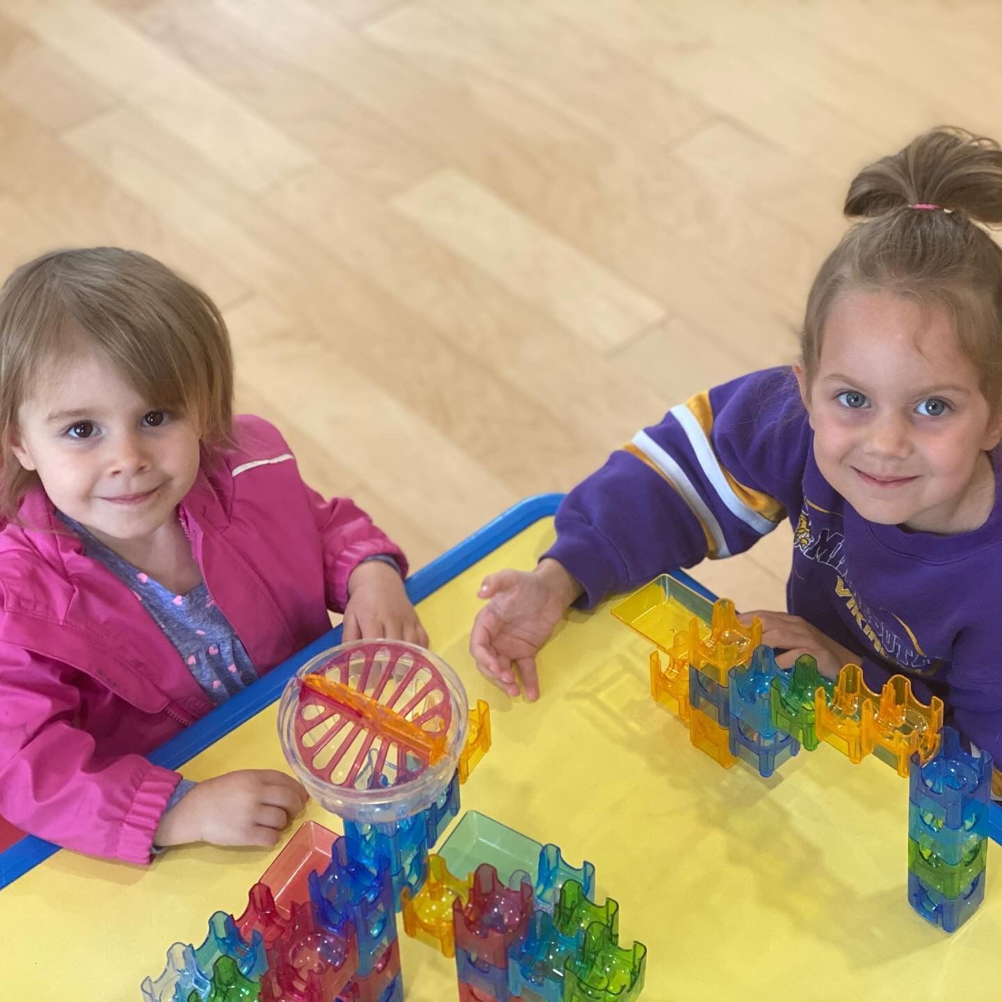 Two young children smiling, building with colorful blocks at a table.