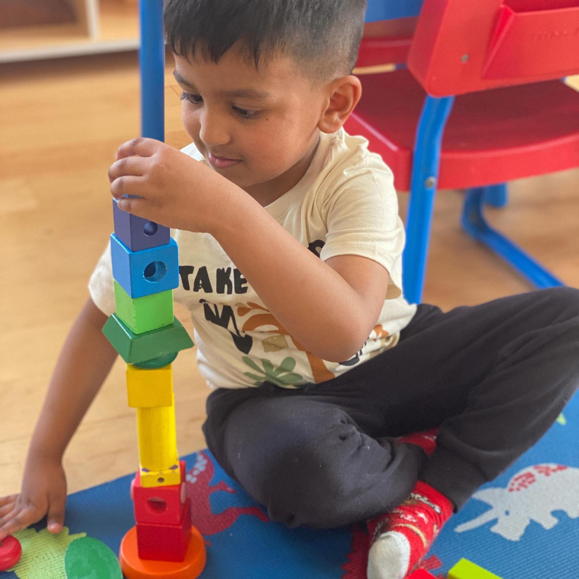 Boy stacking colorful wooden blocks on a mat. Indoors, smiling.