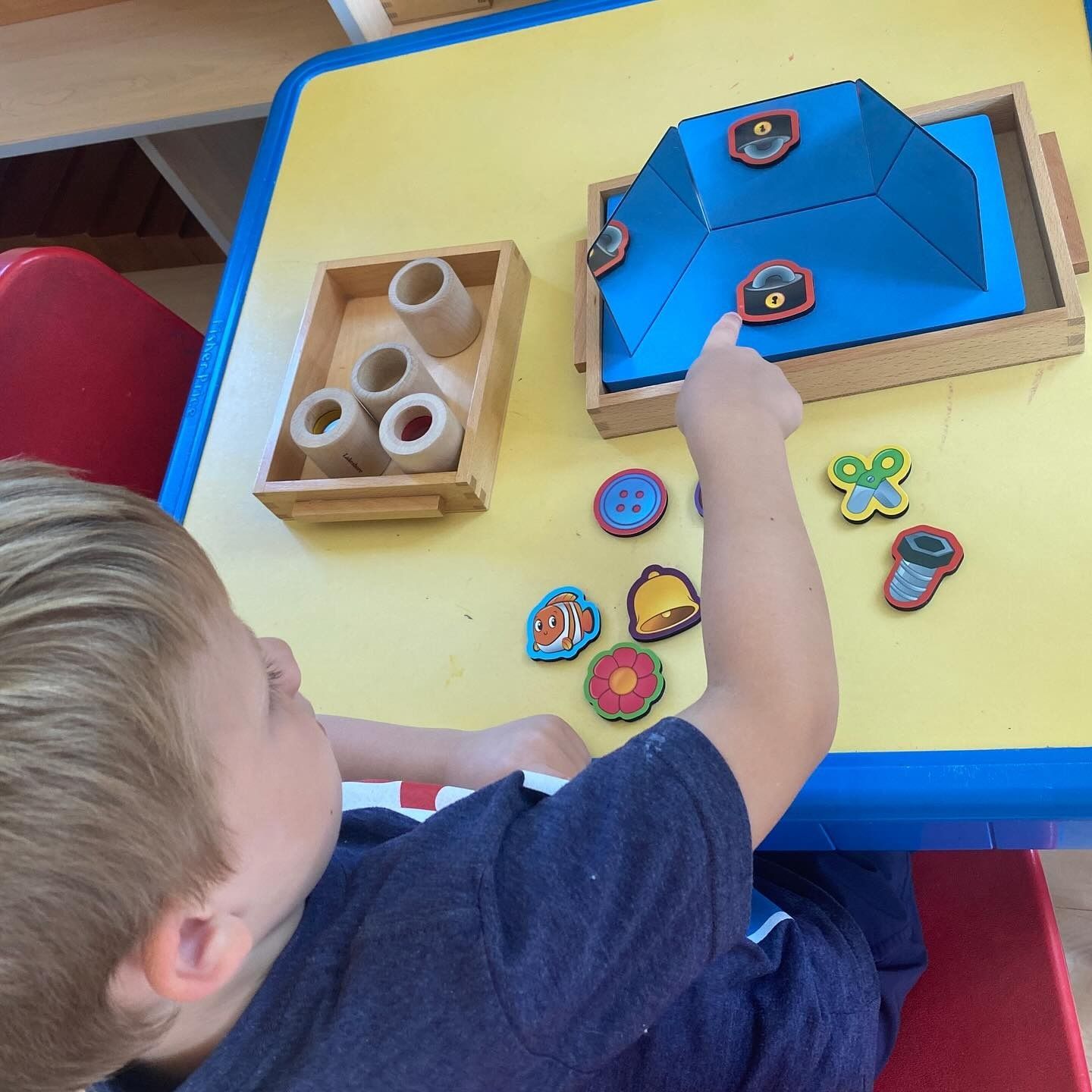 Young child pointing at shapes on a blue surface with wooden toys.