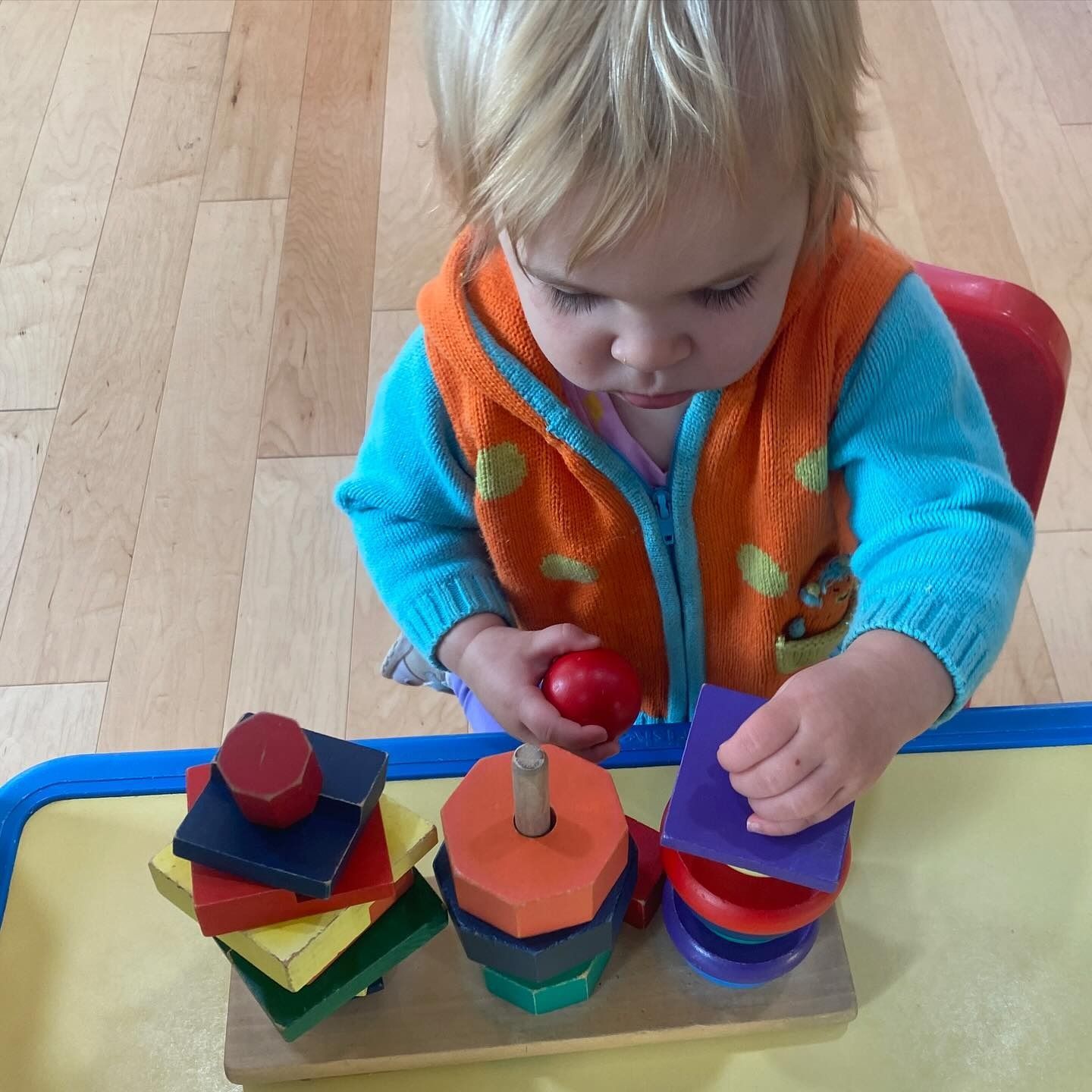 Child stacking colorful wooden blocks on a peg.