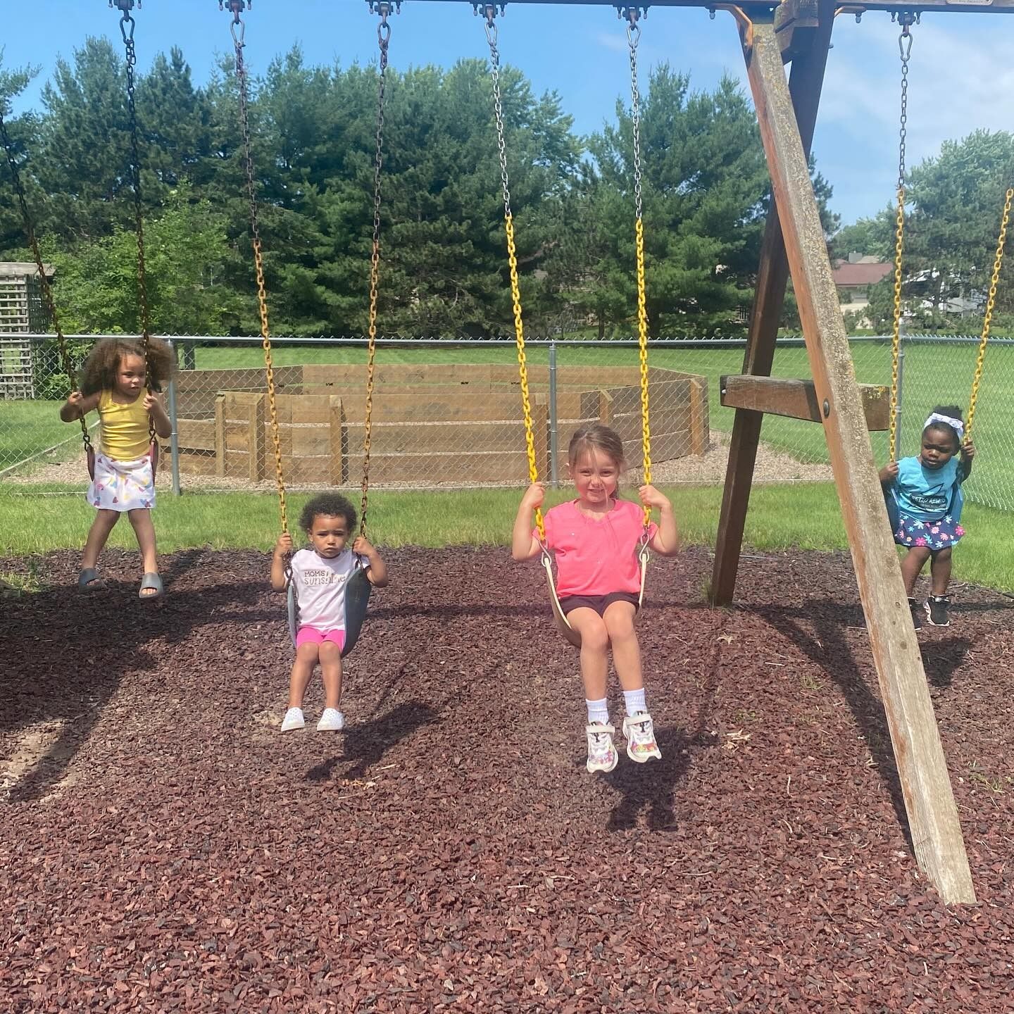 Four children swinging on a playground swing set on a sunny day.