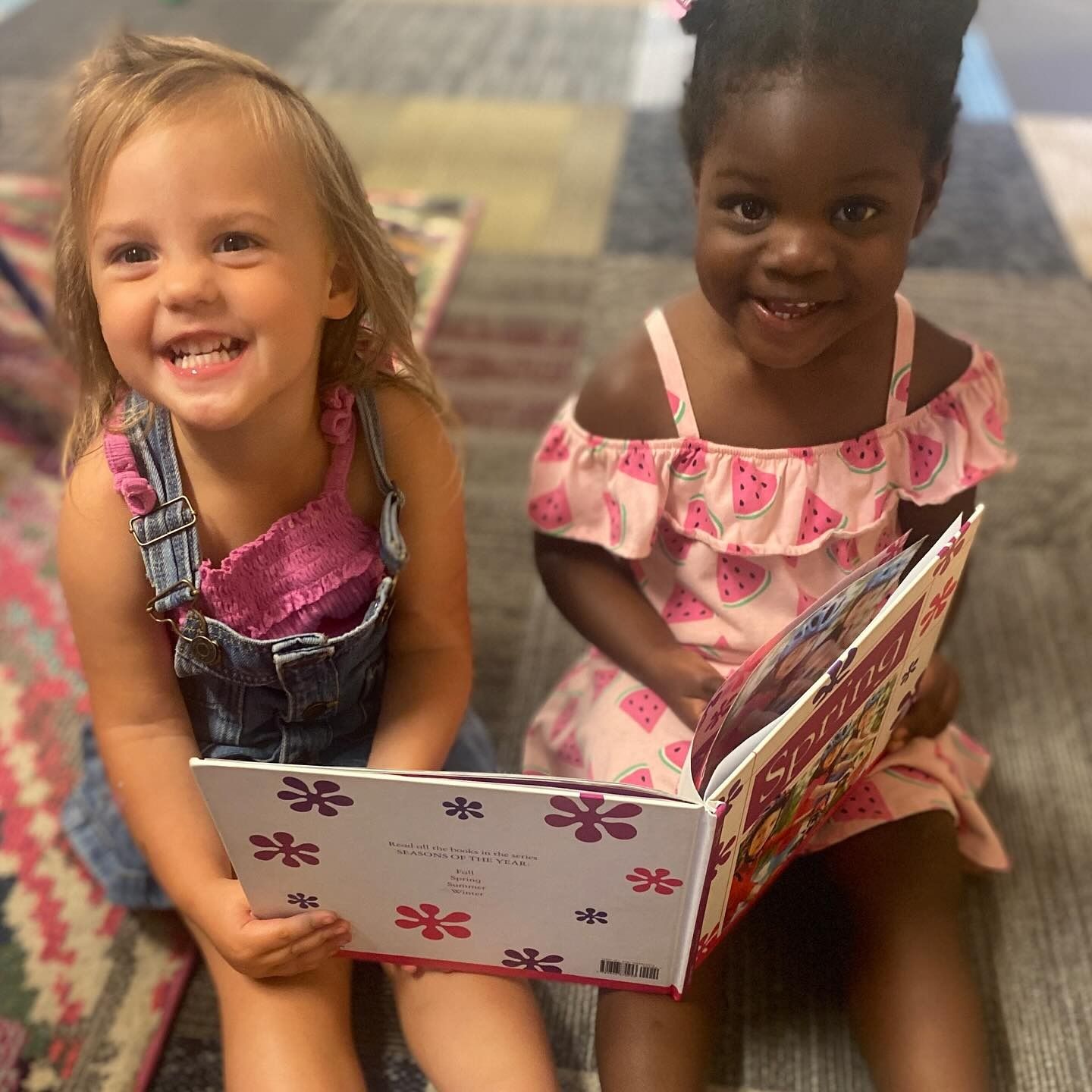 Two young children smiling and reading a book together indoors.