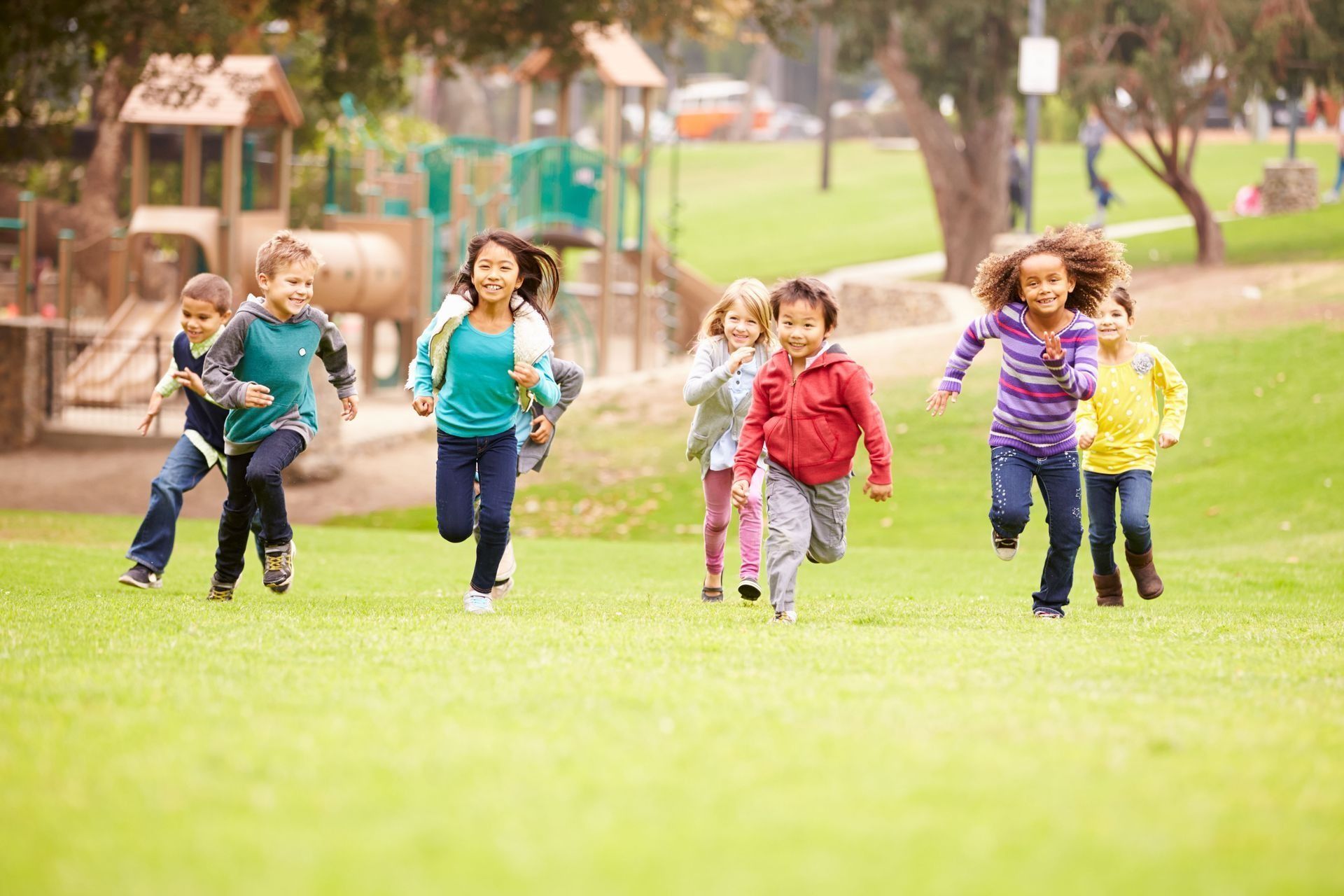 Children running on a grassy field toward a playground.
