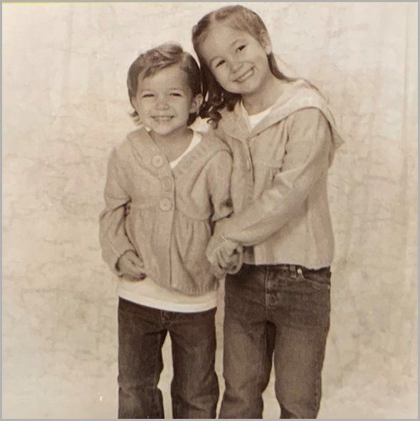 Two smiling children in casual clothes, posing close together against a light background.