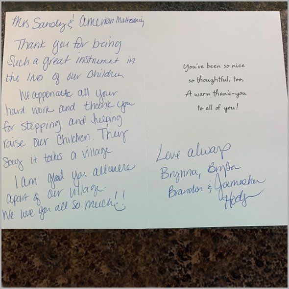 Two children smiling, sitting in a tree. The boy wears a blue shirt and denim shorts, the girl a white shirt.